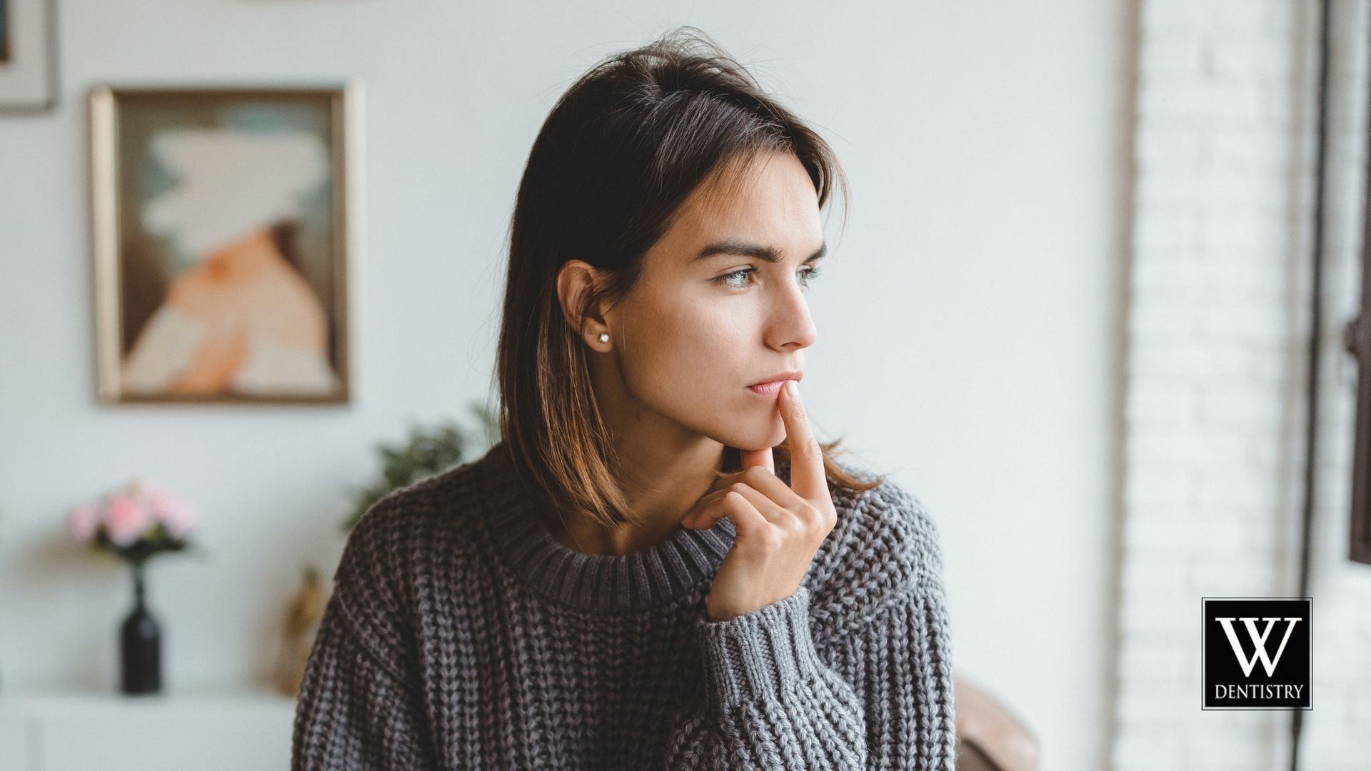 A woman in a sweater is looking out of a window.