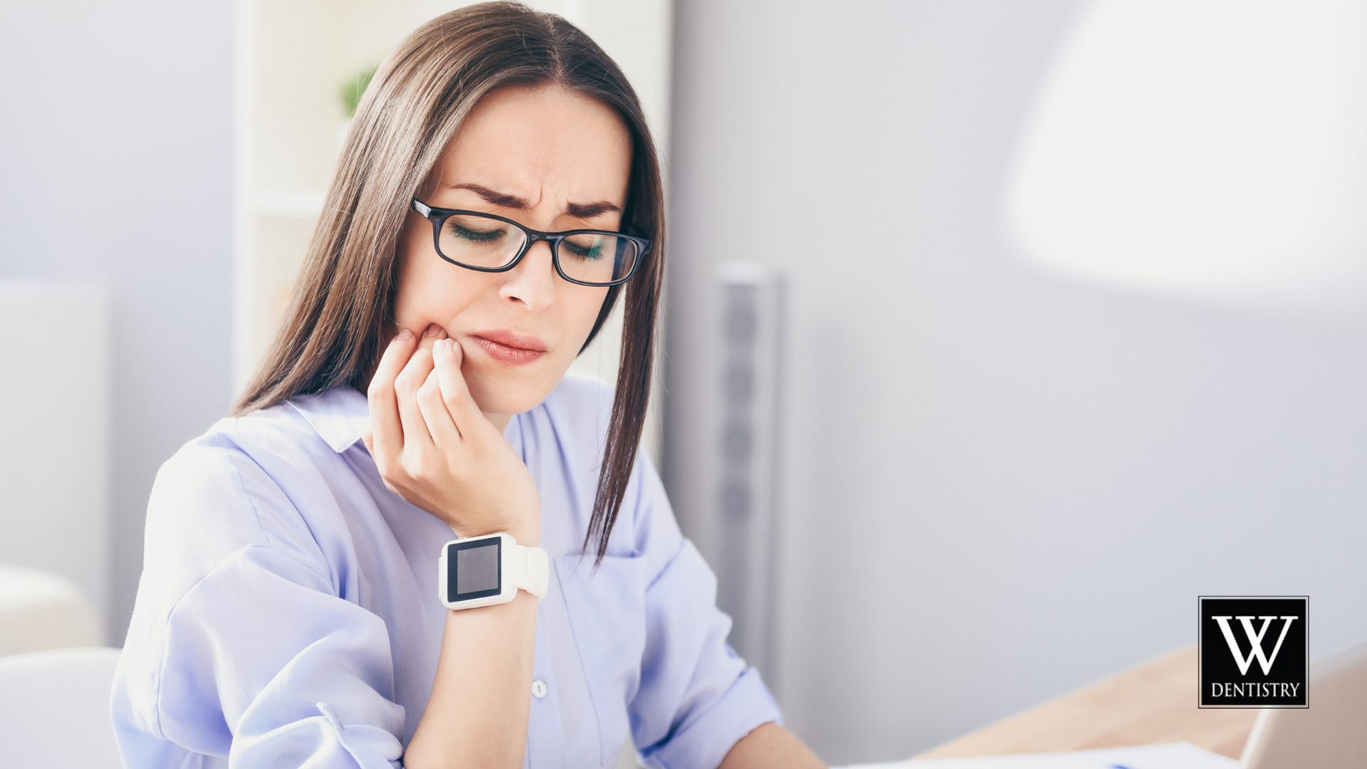 Woman with glasses touching her cheek, showing signs of tooth pain while wearing a smartwatch.
