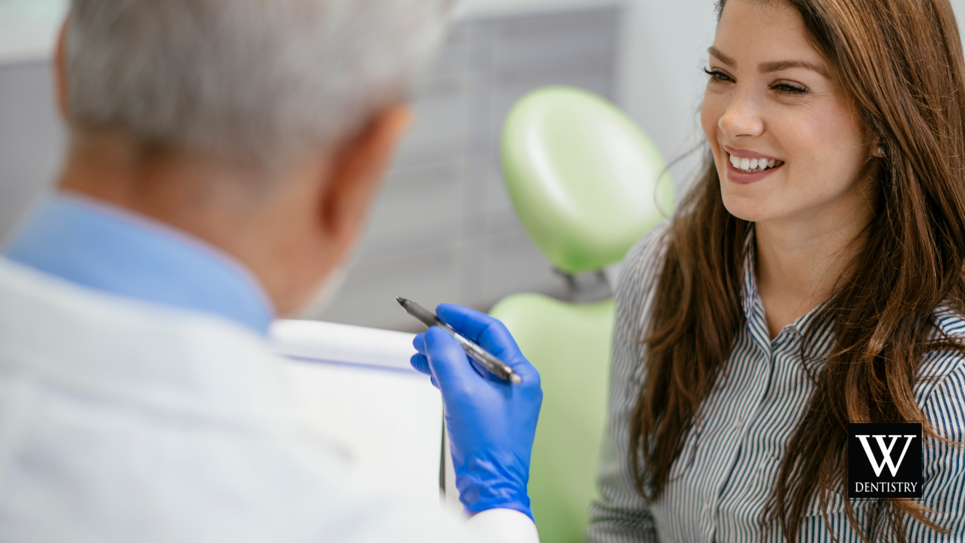 Dentist talking with a smiling patient in a dental office. The dentist is holding a pen and clipboard.