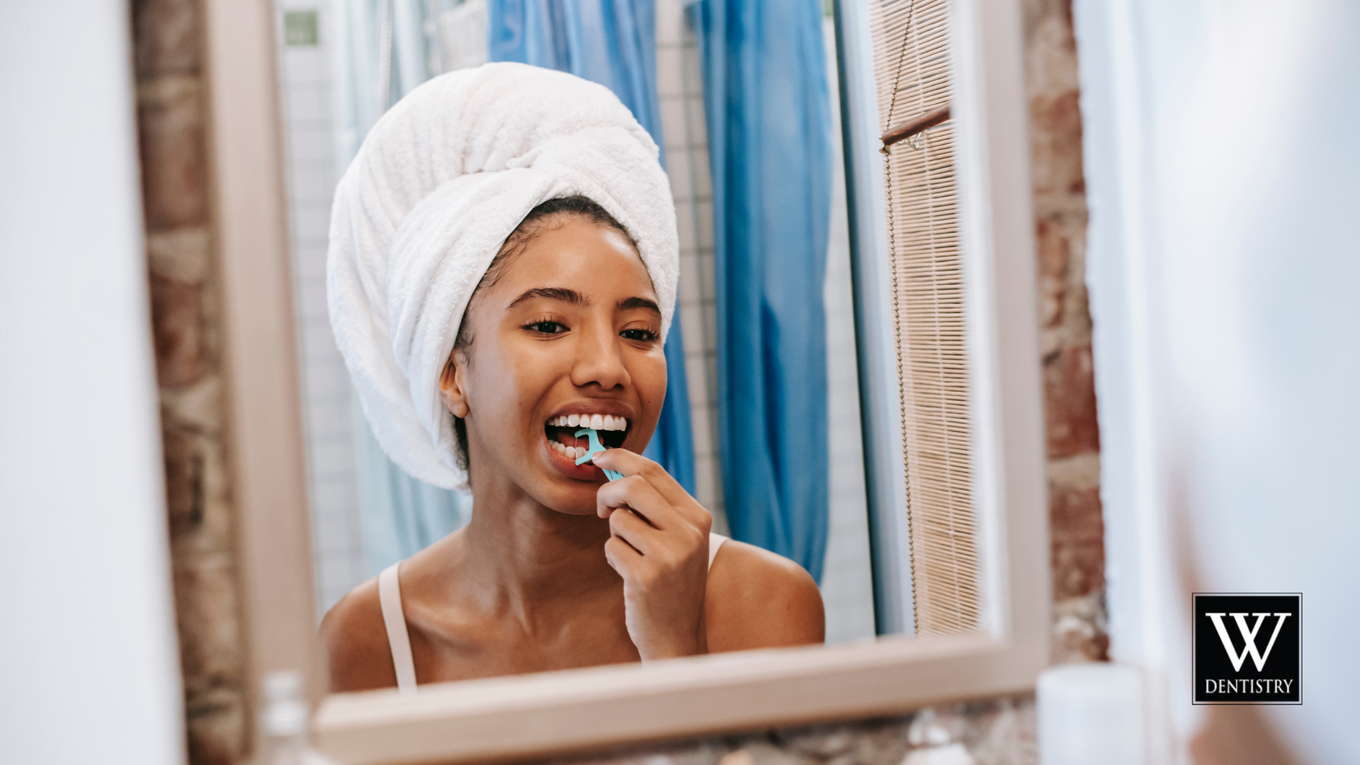 A woman with a towel wrapped around her head is brushing her teeth in front of a mirror.