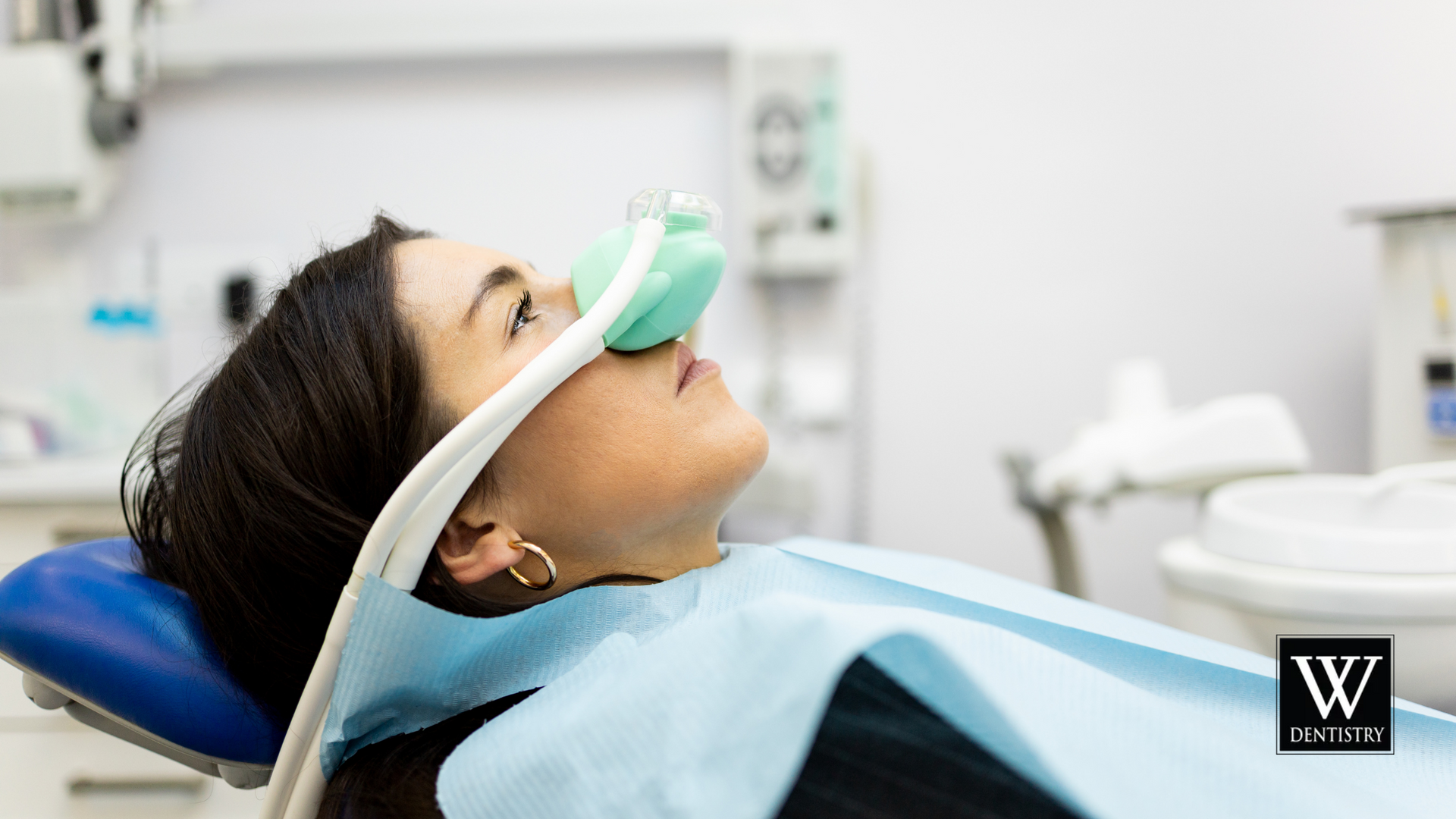 A woman is laying in a dental chair with an oxygen mask on her face.