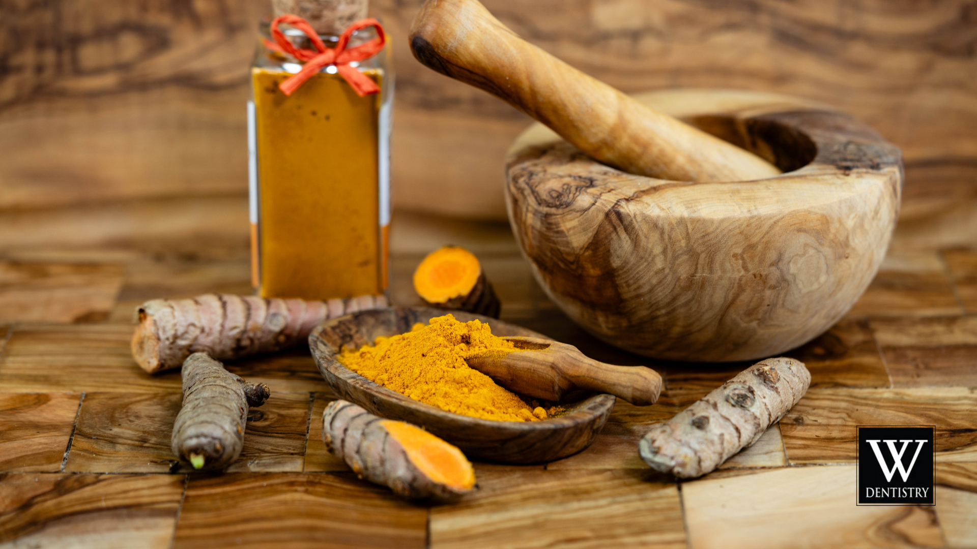 A mortar and pestle , turmeric , and a bottle of turmeric powder on a wooden table.