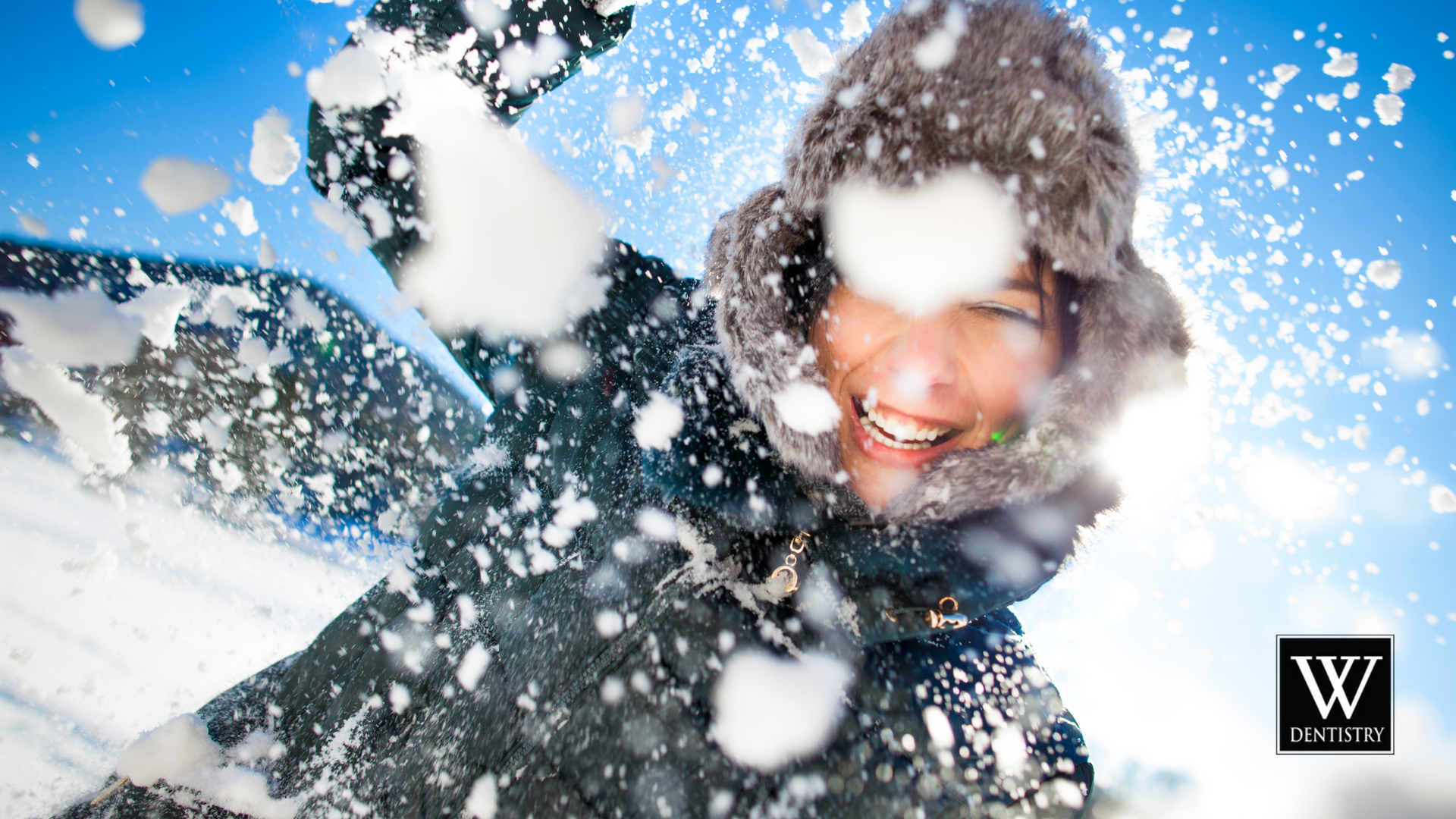 A woman is throwing snow in the air and smiling.