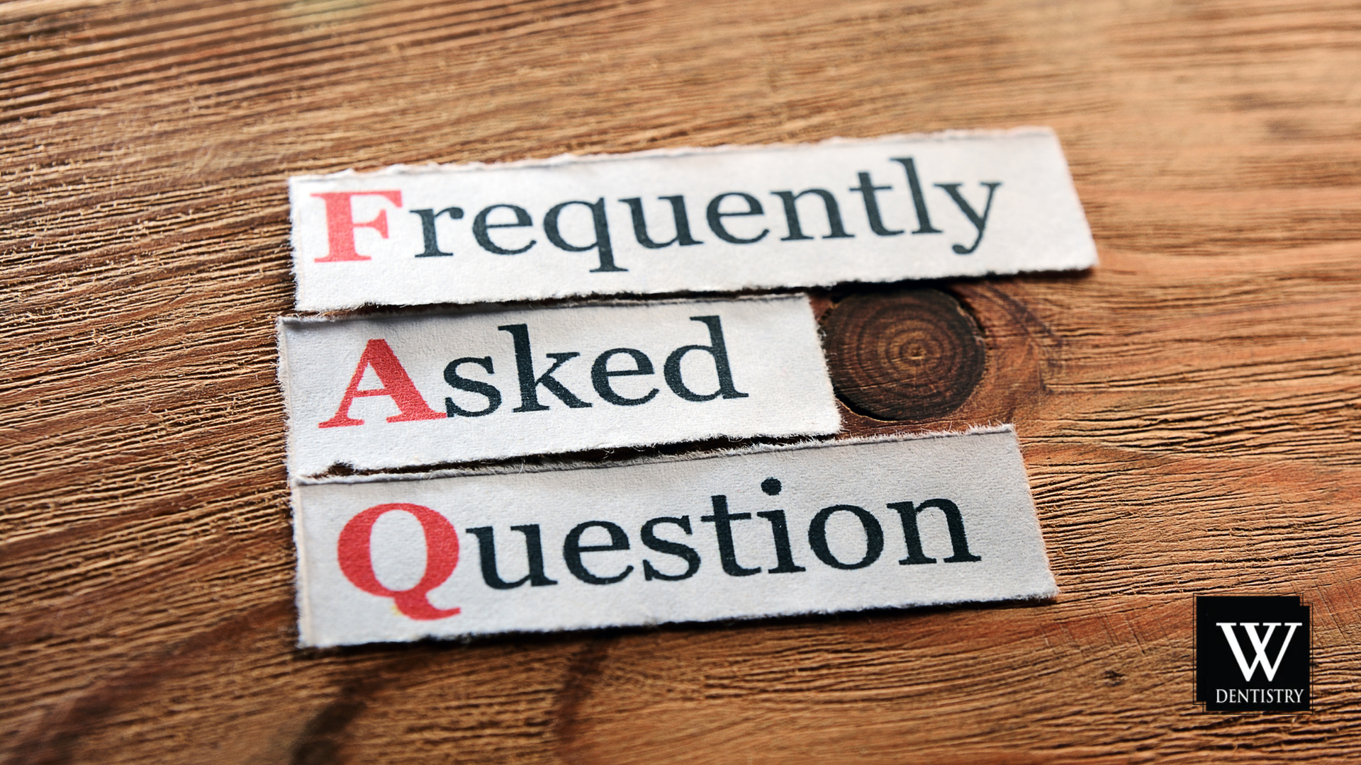 Three pieces of paper with the words frequently asked questions written on them on a wooden table.