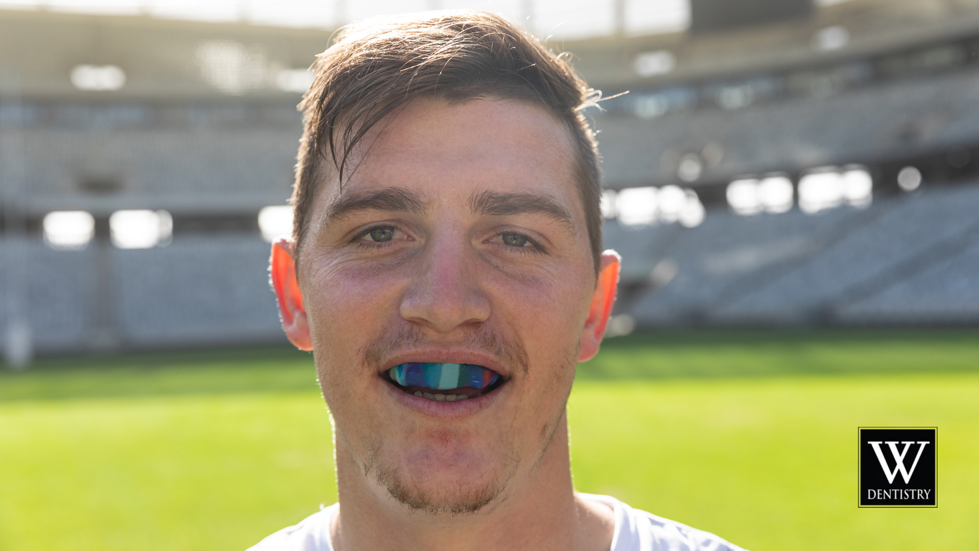 A man with braces on his teeth is standing in front of a stadium.