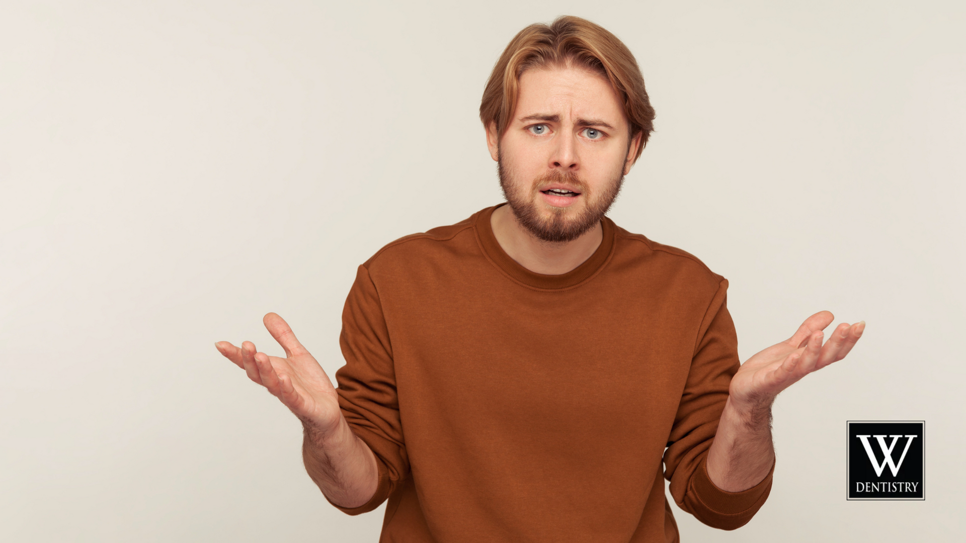 A man in a brown sweater is shrugging his shoulders.