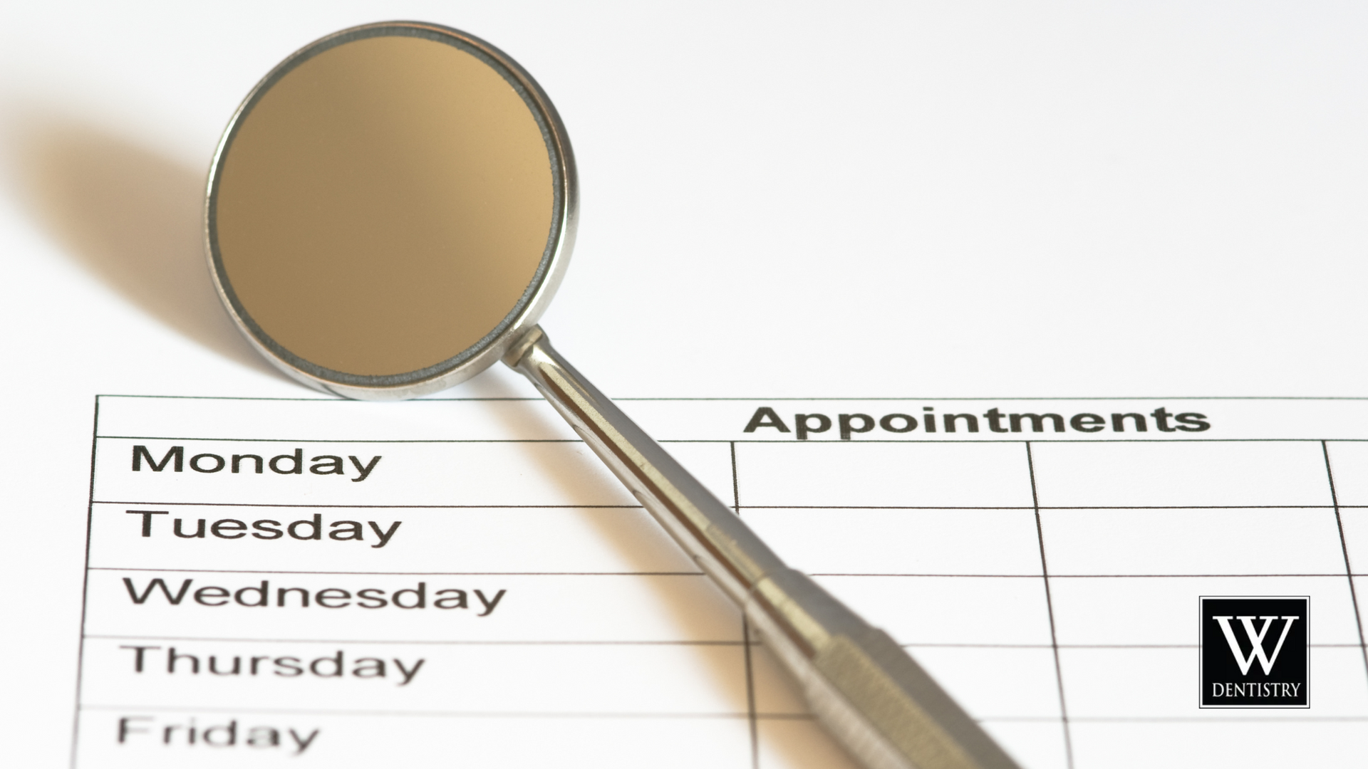 A dental mirror is sitting on top of a dental appointment schedule