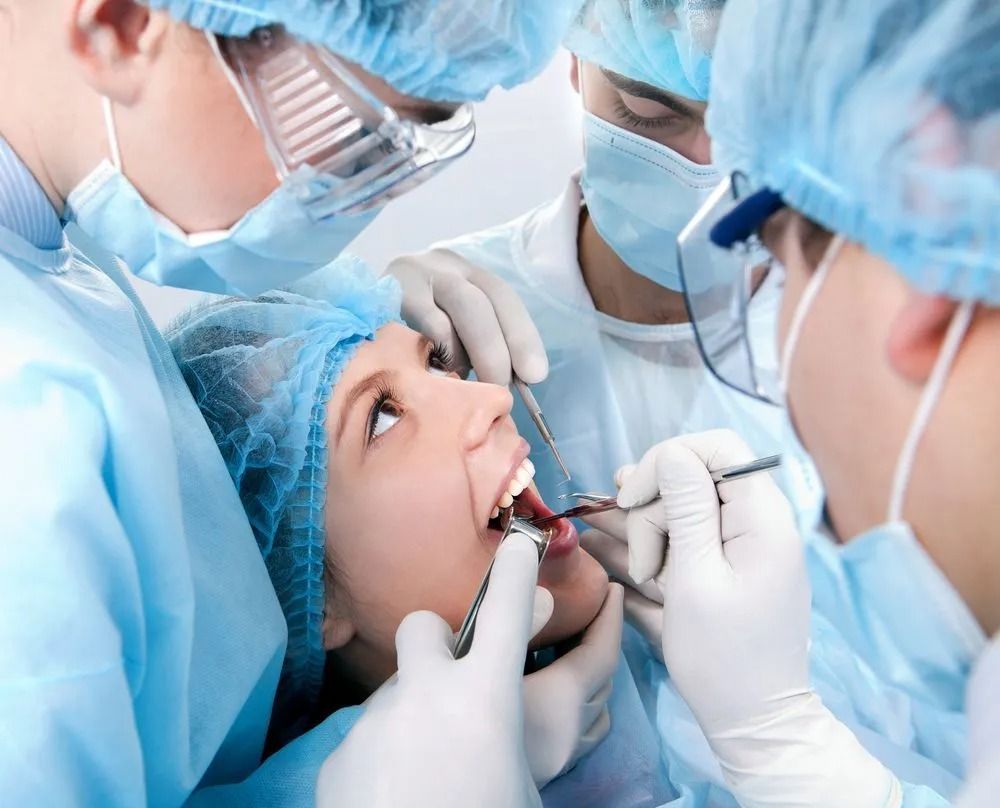 Dental team treating a patient during an oral procedure, with gloved hands and surgical masks in a clinical setting