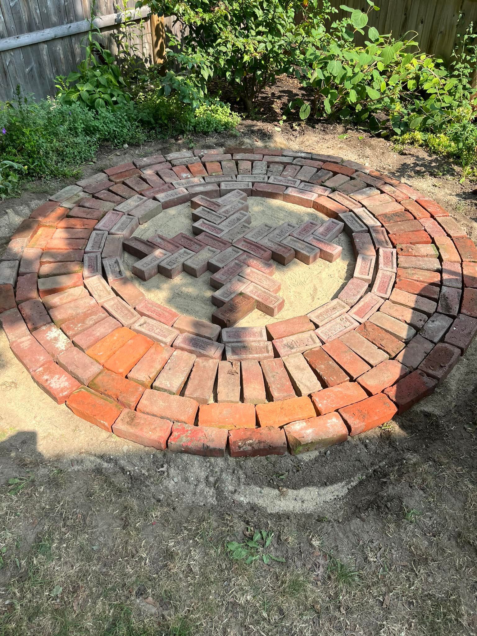 A circle of bricks is sitting on the ground in a garden.