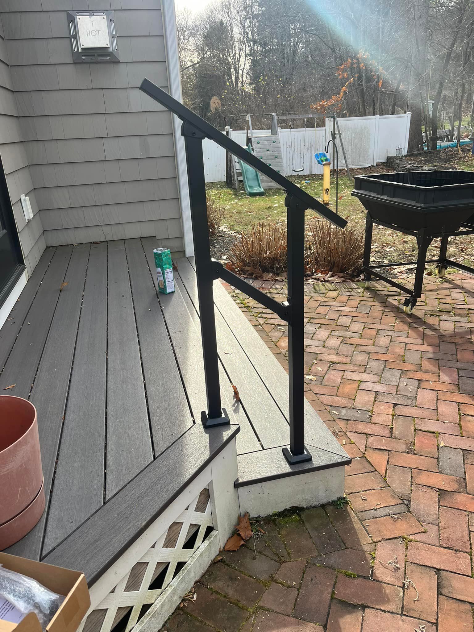 A black railing on a deck next to a brick patio.