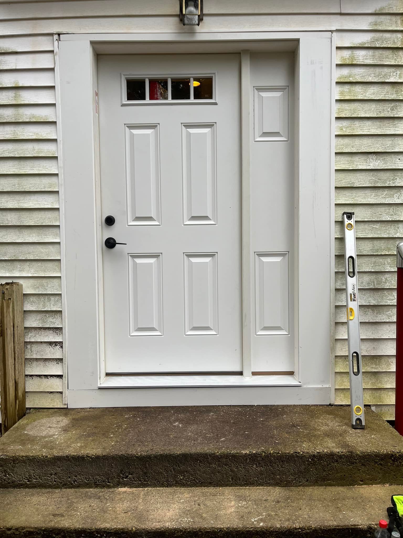 A white door is sitting on the side of a house next to a level.