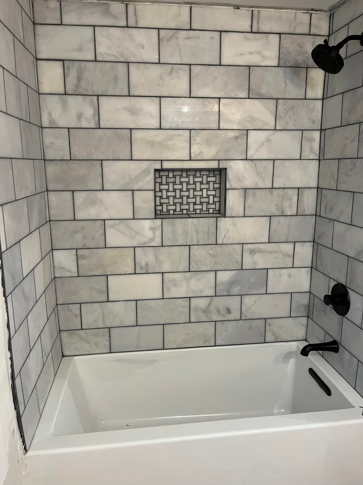 There is a bathtub in the shower with marble tiles on the wall.
