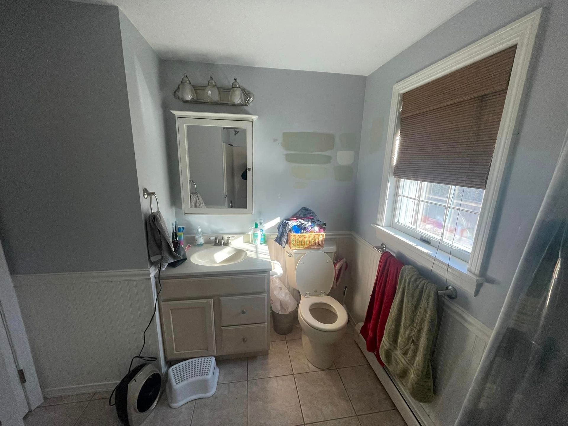 A bathroom with a toilet , sink , mirror and window.