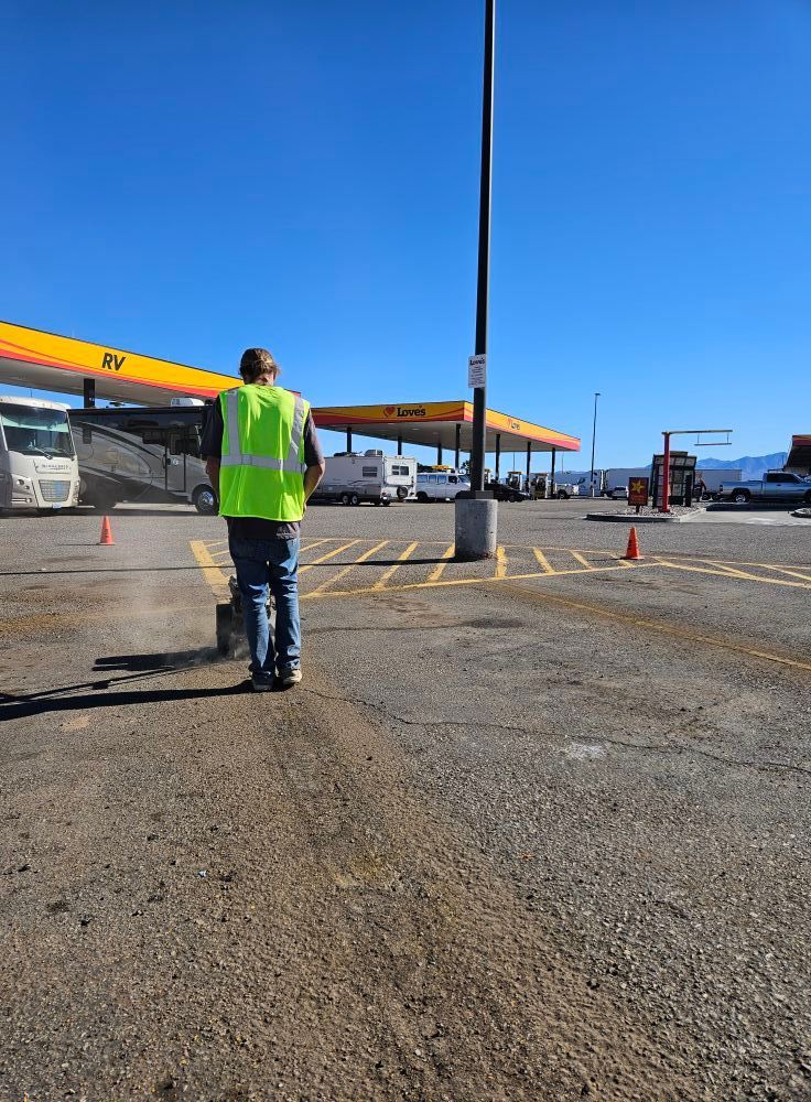 Person in neon vest walking across a gas station lot under a clear blue sky.