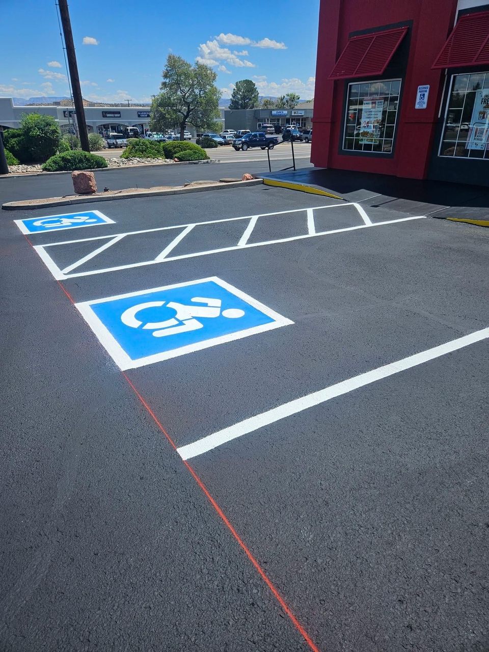 Accessible parking spaces and cross-hatched no-parking zone beside a red building on a sunny day
