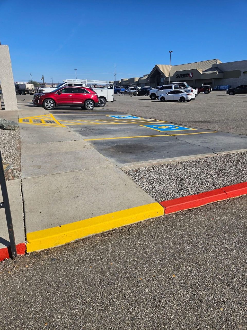 Accessible parking spaces and curb ramp outside a building, with cars in the lot under a clear sky.