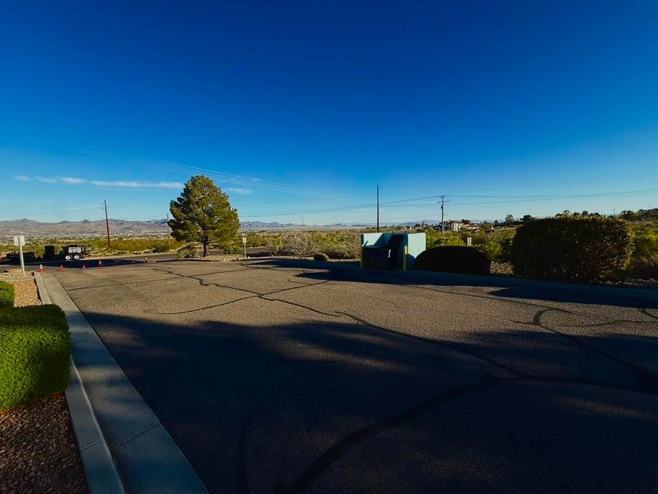 Empty parking lot beside a road under a clear blue sky with distant hills and trees