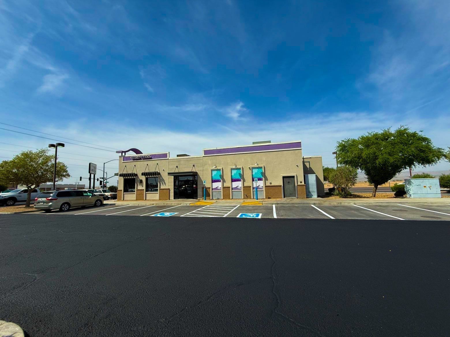 Small beige storefront with blue signs, empty parking lot, and a clear blue sky.