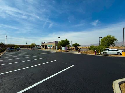 Empty parking lot with white parking lines, a few cars, and buildings under a blue sky