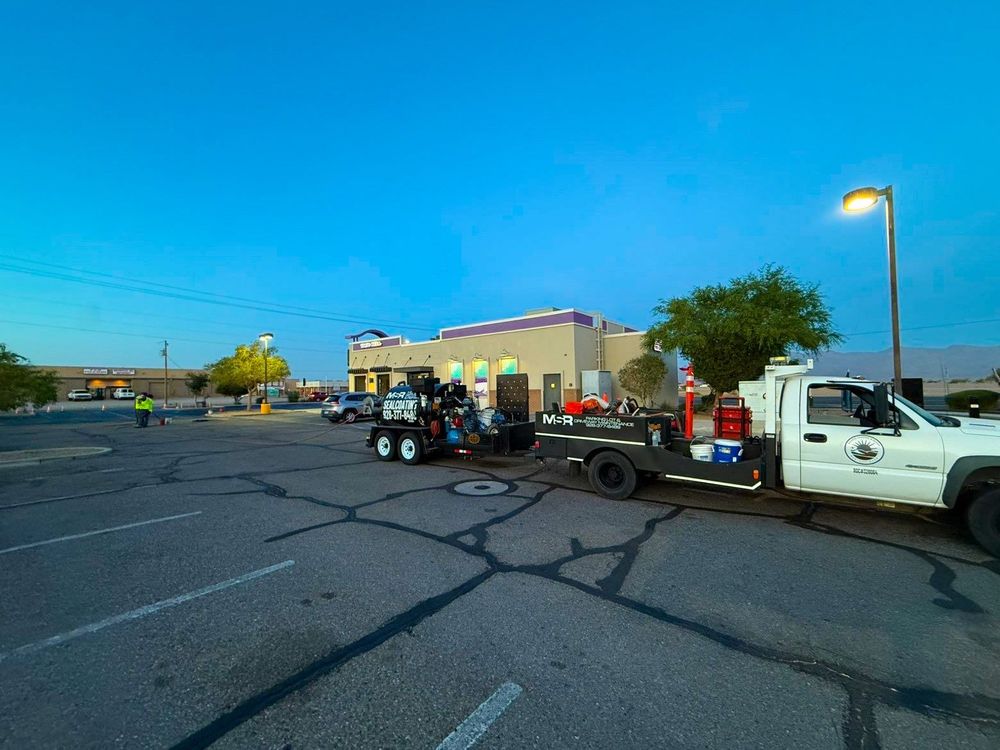 Pickup truck towing a trailer in a cracked parking lot beside a small building at dusk