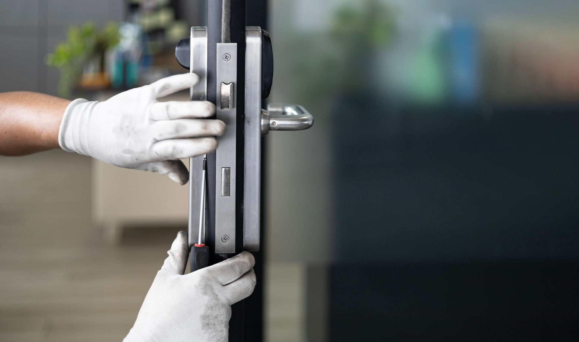 Hands in gloves adjusting a glass door handle lock with a screwdriver.
