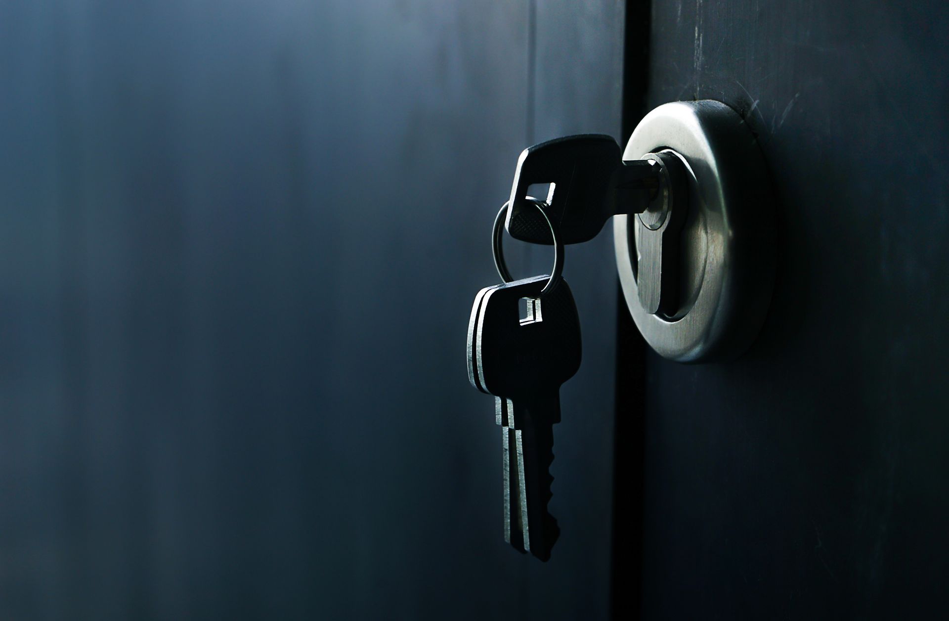 Close-up to a pair of keys, one of them being inserted into a silver lock in a door.