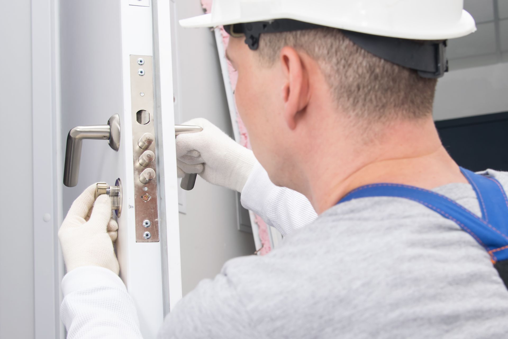 Worker installing a metal door lock with gloves and tools.