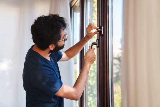 A man in a blue shirt is fixing a window handle with a screwdriver.