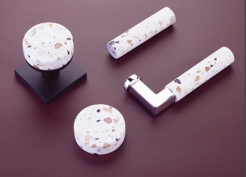 Door hardware with terrazzo-patterned handles and knob, set against a burgundy background.