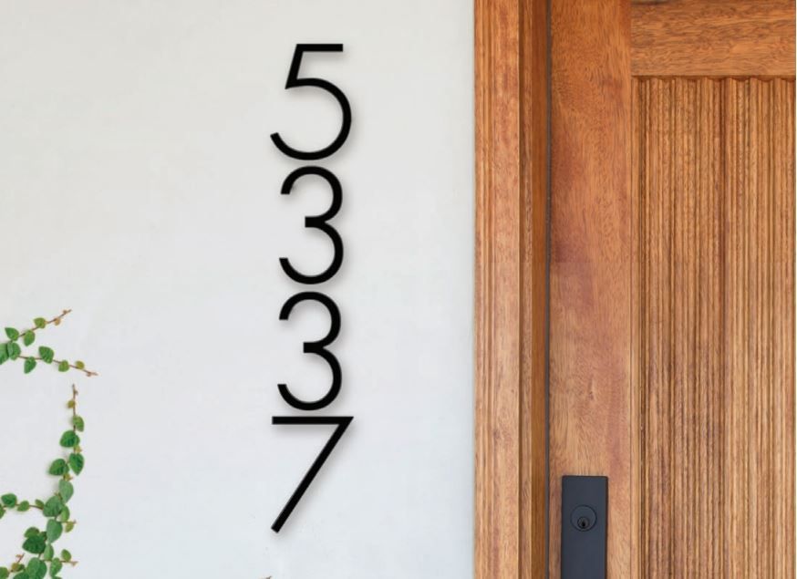Black address numbers 5337 vertically mounted on a white wall next to a wooden door.