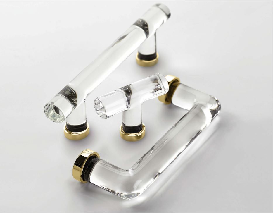 Clear acrylic cabinet handles with gold and black accents on a white surface.