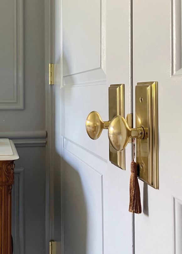 White door with gold hardware. A tassel hangs from the door handle.