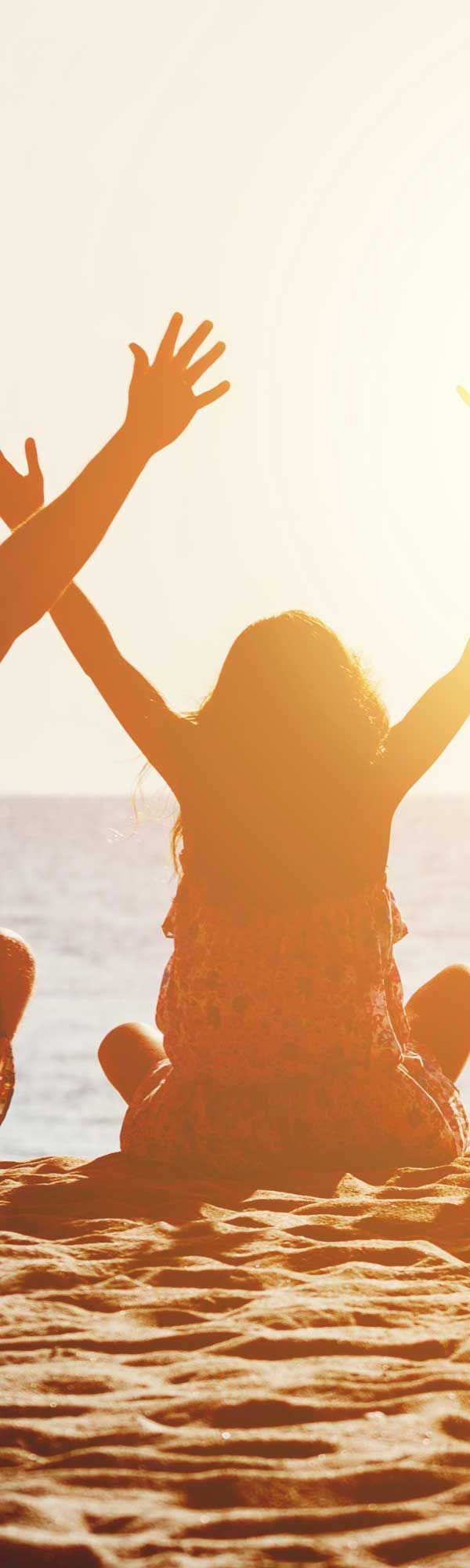 Silhouetted people with arms raised in joy on a beach with the bright sun behind.