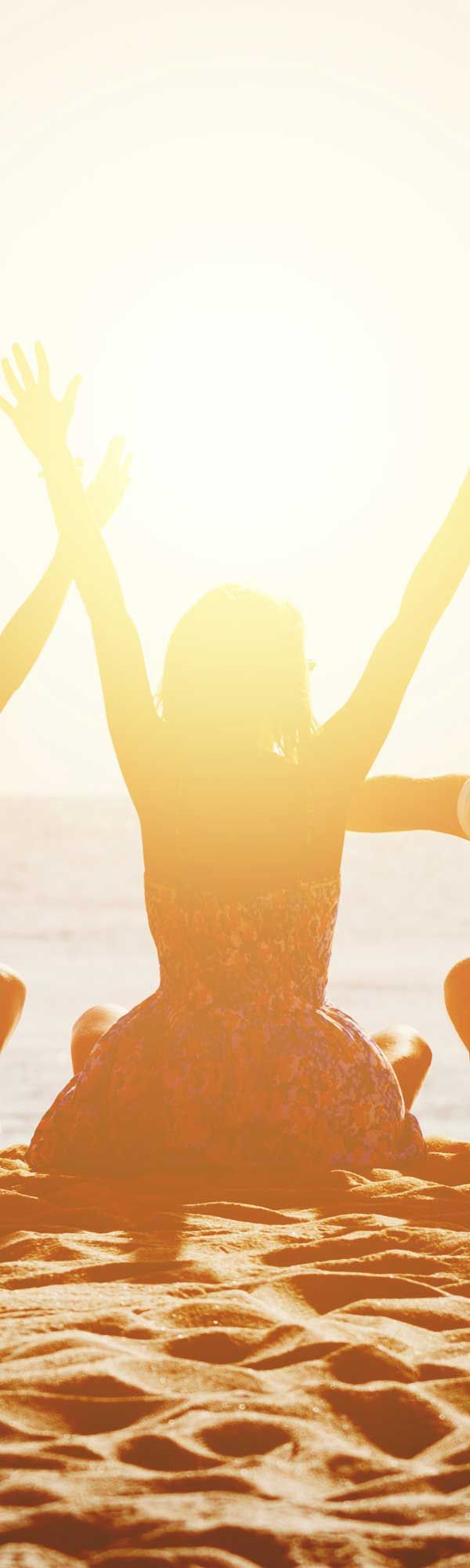 People with arms raised in front of a bright sun.