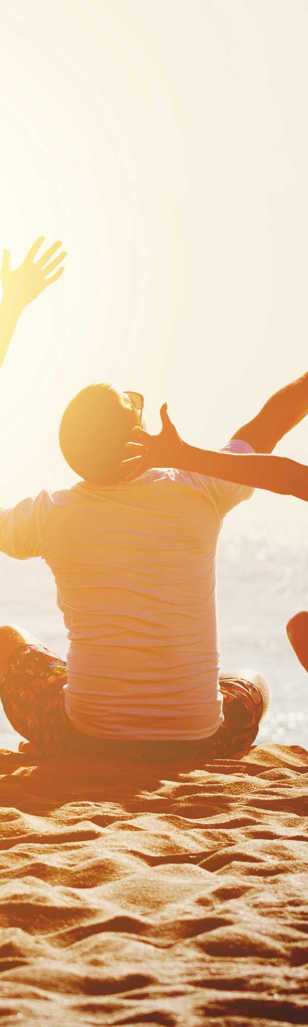 People reaching up on a beach, silhouetted against a bright sky. Arms raised, celebrating or greeting the sun.
