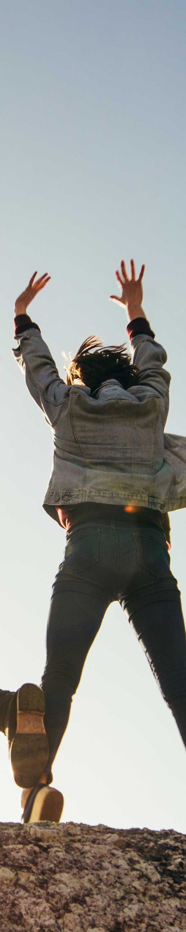 Person jumping in the air, arms raised. Overcast sky in background.