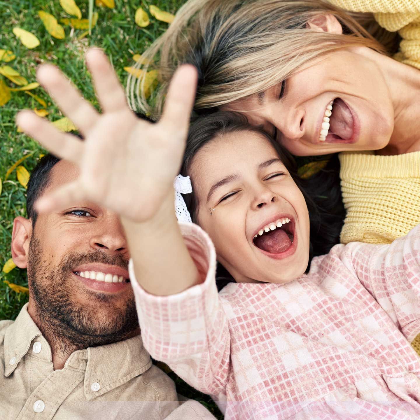 Family lying in grass, smiling and laughing. Girl waves hand at camera. Family lying in grass, smiling and laughing. Girl waves hand at camera.
