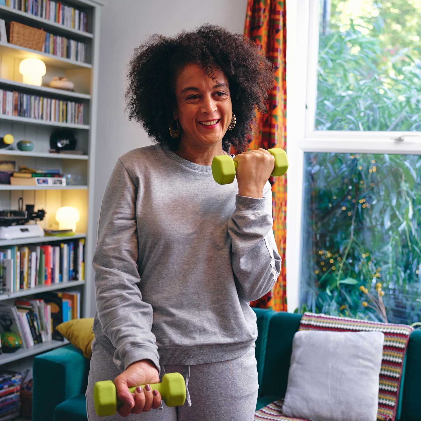 Woman exercising with dumbbells indoors, smiling. She wears gray sweats. Bright green weights. Woman exercising with dumbbells indoors, smiling. She wears gray sweats. Bright green weights.