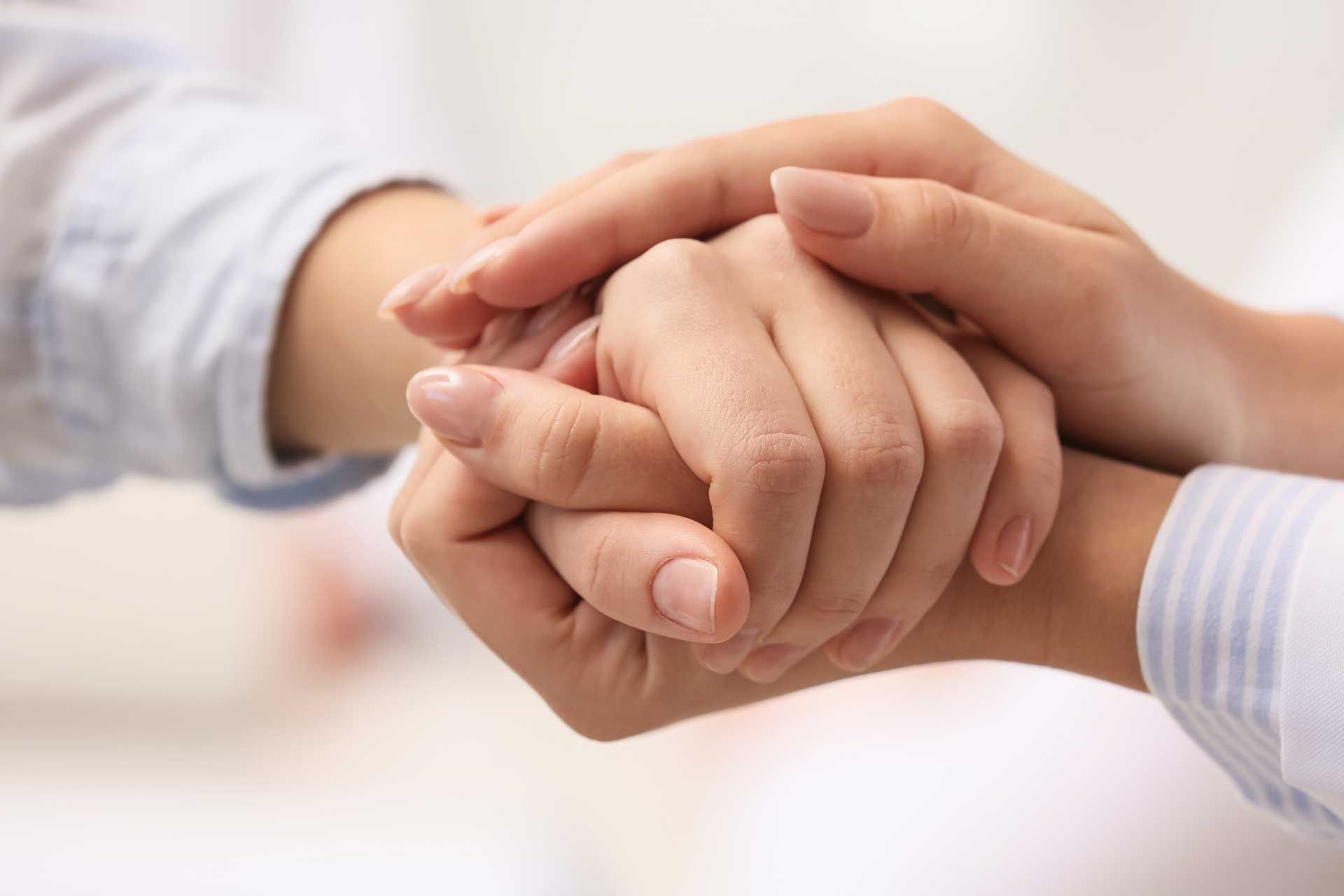 Hands clasped together, one resting on top of the other, offering comfort or support. Hands clasped together, one resting on top of the other, offering comfort or support.