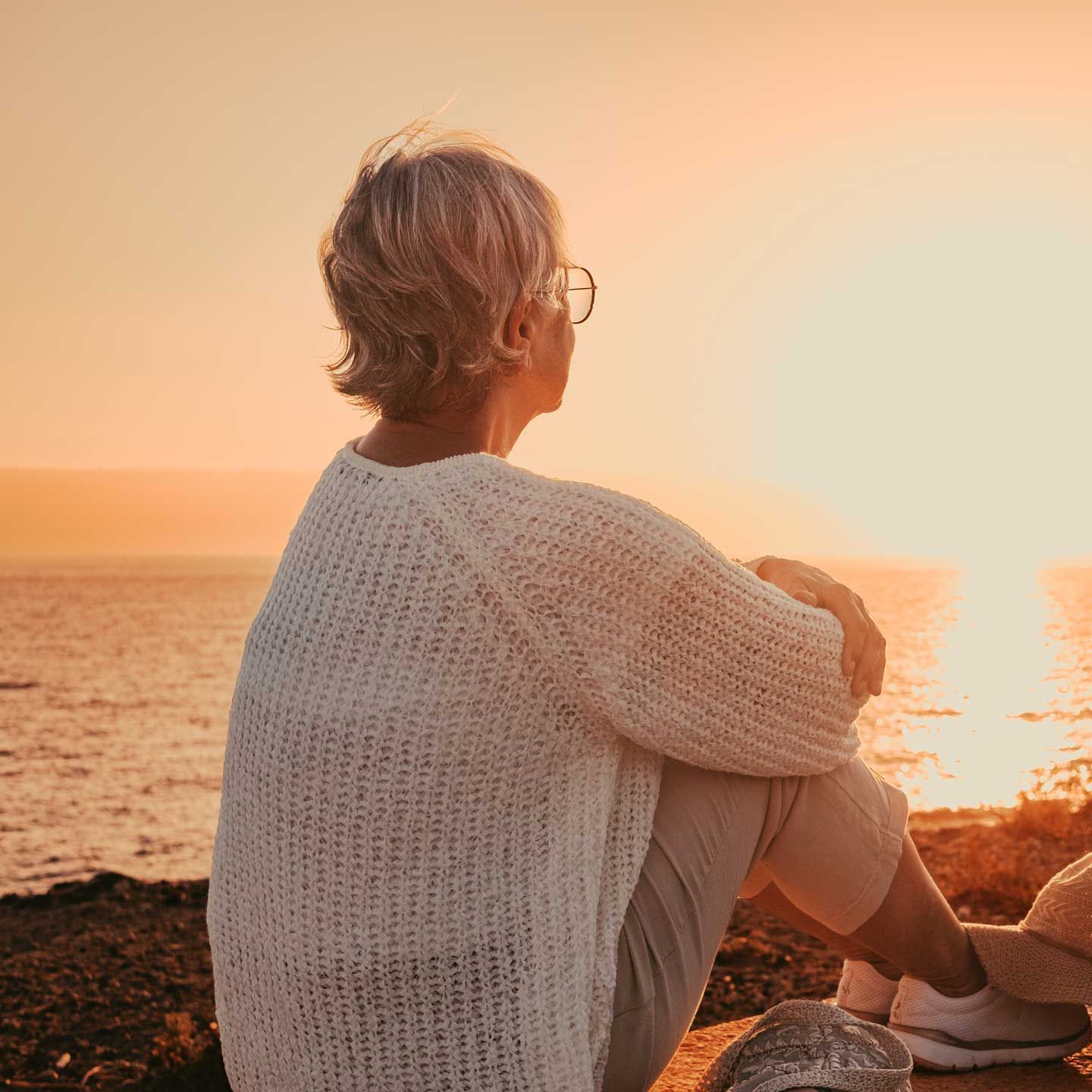 Woman in sweater looks at sunset over ocean. Woman in sweater looks at sunset over ocean.