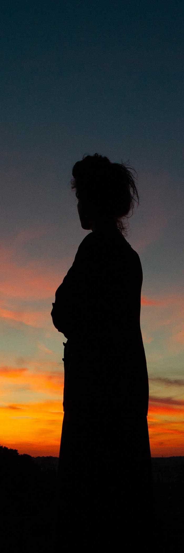Silhouette of a person with arms crossed, set against an orange and blue sunset.