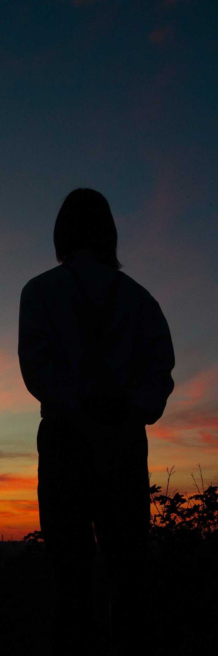 Silhouette of a person standing at dusk, with a colorful sky.