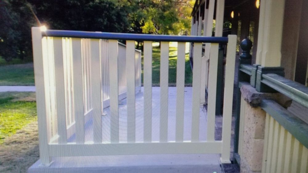 A White Fence With A Black Railing Is Surrounding A Porch — Boambee Home Improvements in Bellingen, NSW