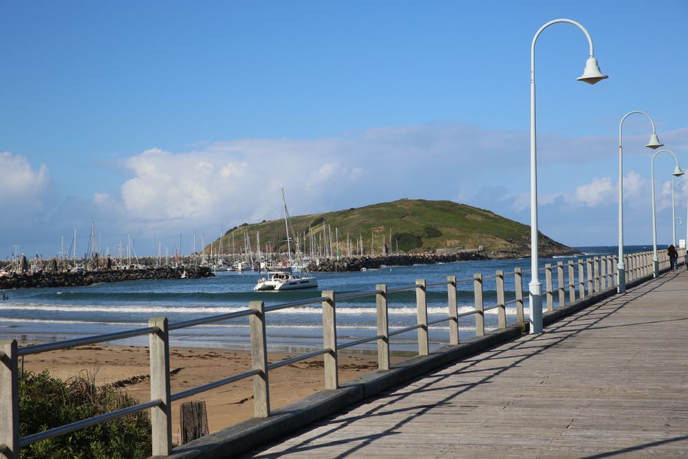 A Pier Leading To A Beach With Boats In The Water — Boambee Home Improvements in Coffs Harbour, NSW