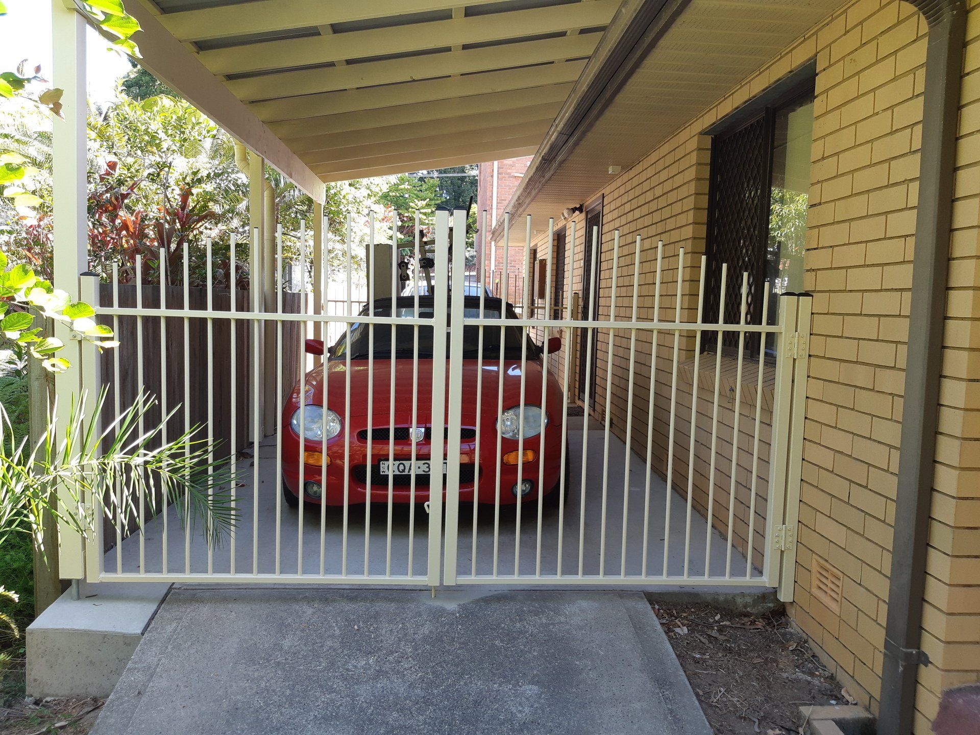 A Red Car Is Parked In A Driveway Under A Canopy — Boambee Home Improvements in Coffs Harbour, NSW