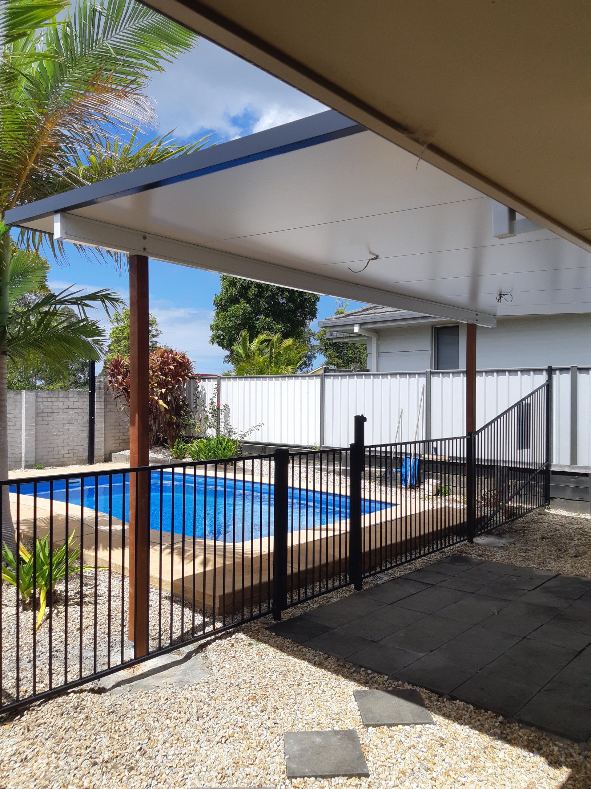 A Swimming Pool Is Surrounded By A Fence And A Covered Area — Boambee Home Improvements in Coffs Harbour, NSW