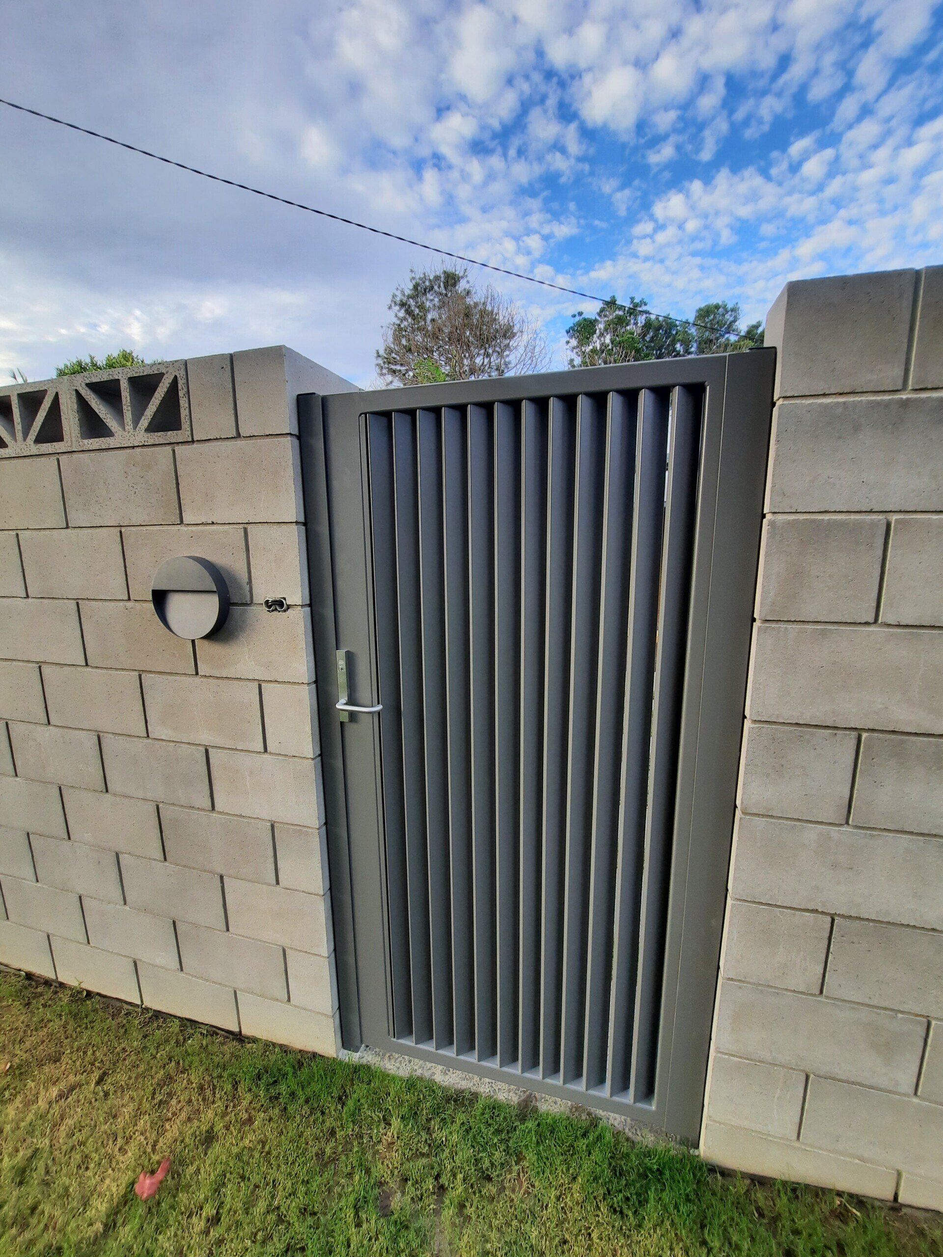 A Brick Wall With A Metal Gate In Front Of It — Boambee Home Improvements in Coffs Harbour, NSW