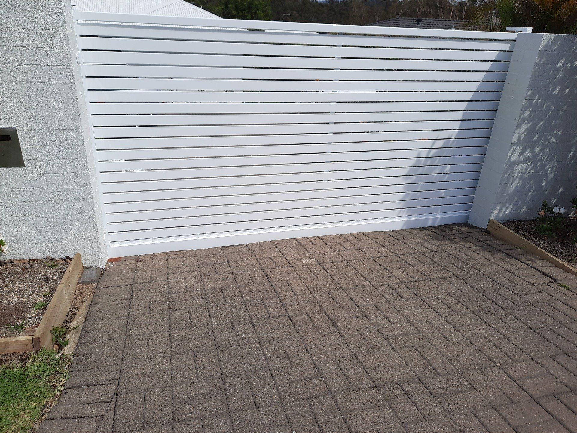 A White Fence Is Sitting On A Brick Driveway Next To A Brick Wall — Boambee Home Improvements in Coffs Harbour, NSW