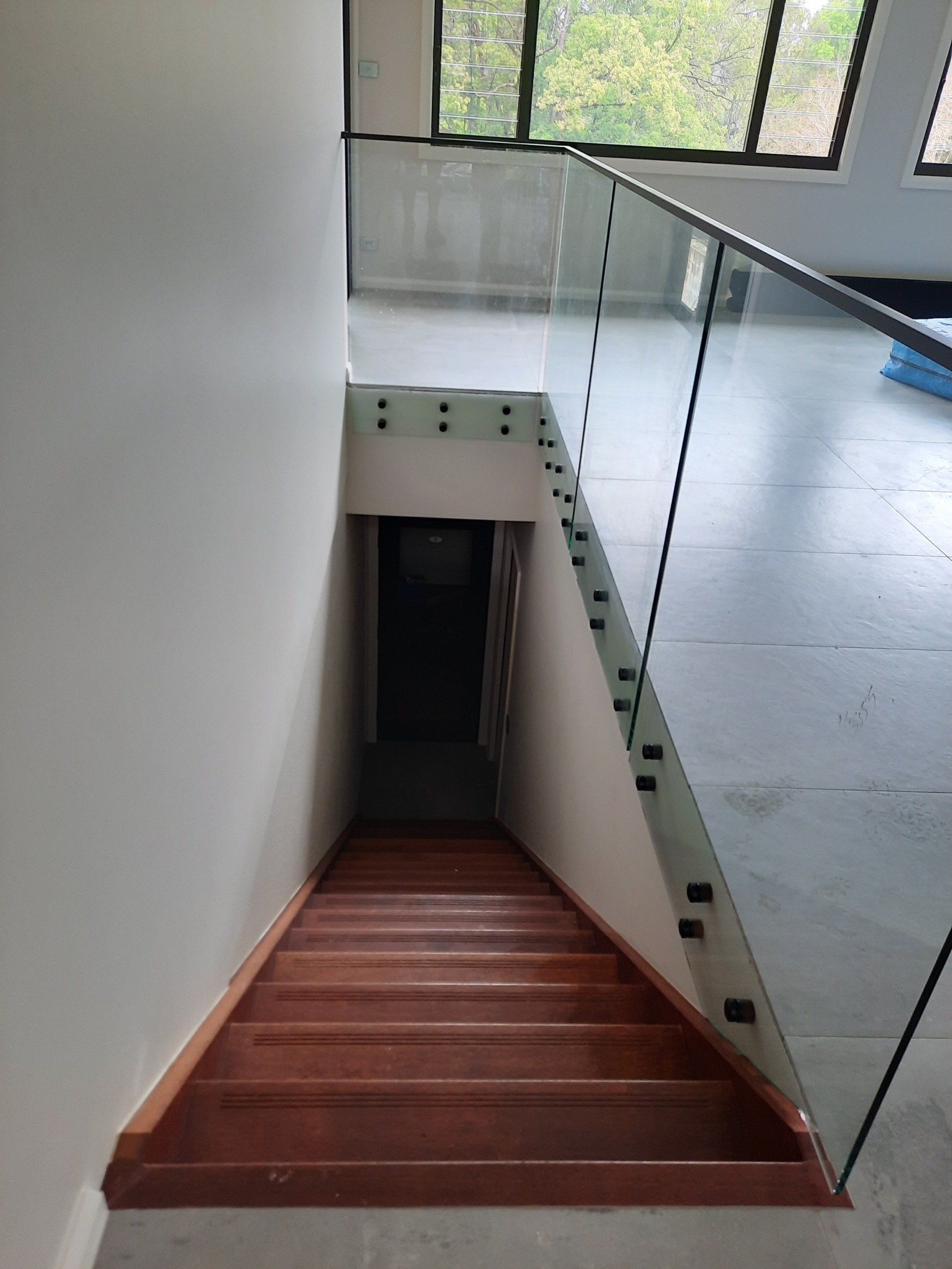 A Wooden Staircase With A Glass Railing Leading Up To The Second Floor.— Boambee Home Improvements in Coffs Harbour, NSW