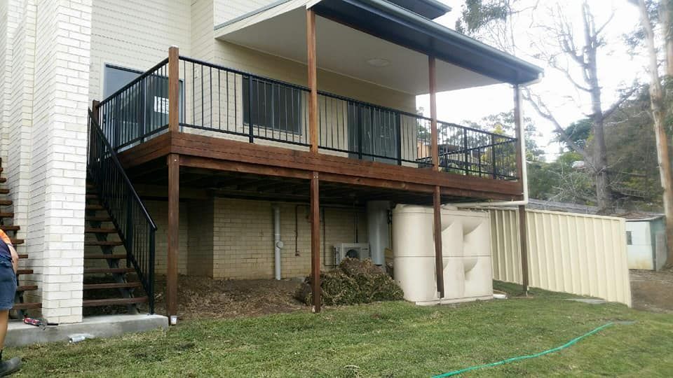 A Man Is Standing In Front Of A House With A Deck And Stairs — Boambee Home Improvements in Coffs Harbour, NSW
